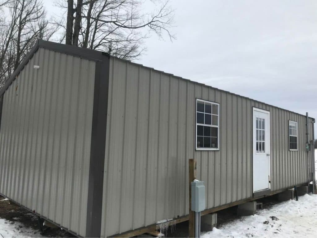 Side of long grey shed with white door and one window