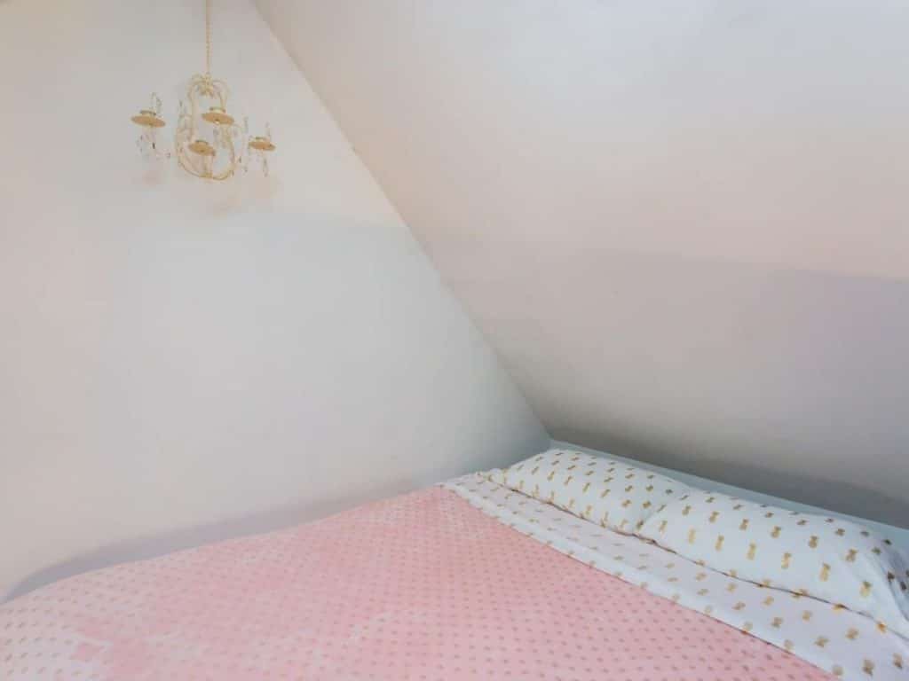Bed under loft ceiling with chandelier light and pink bedding