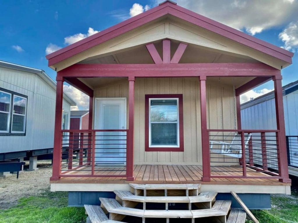 Tan and maroon tiny house with covered porch on lot