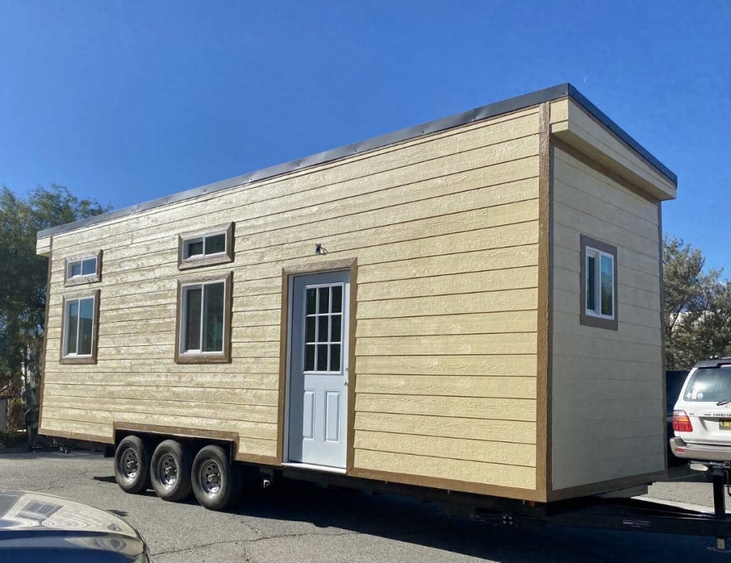 Tan tiny house on wheels with white door