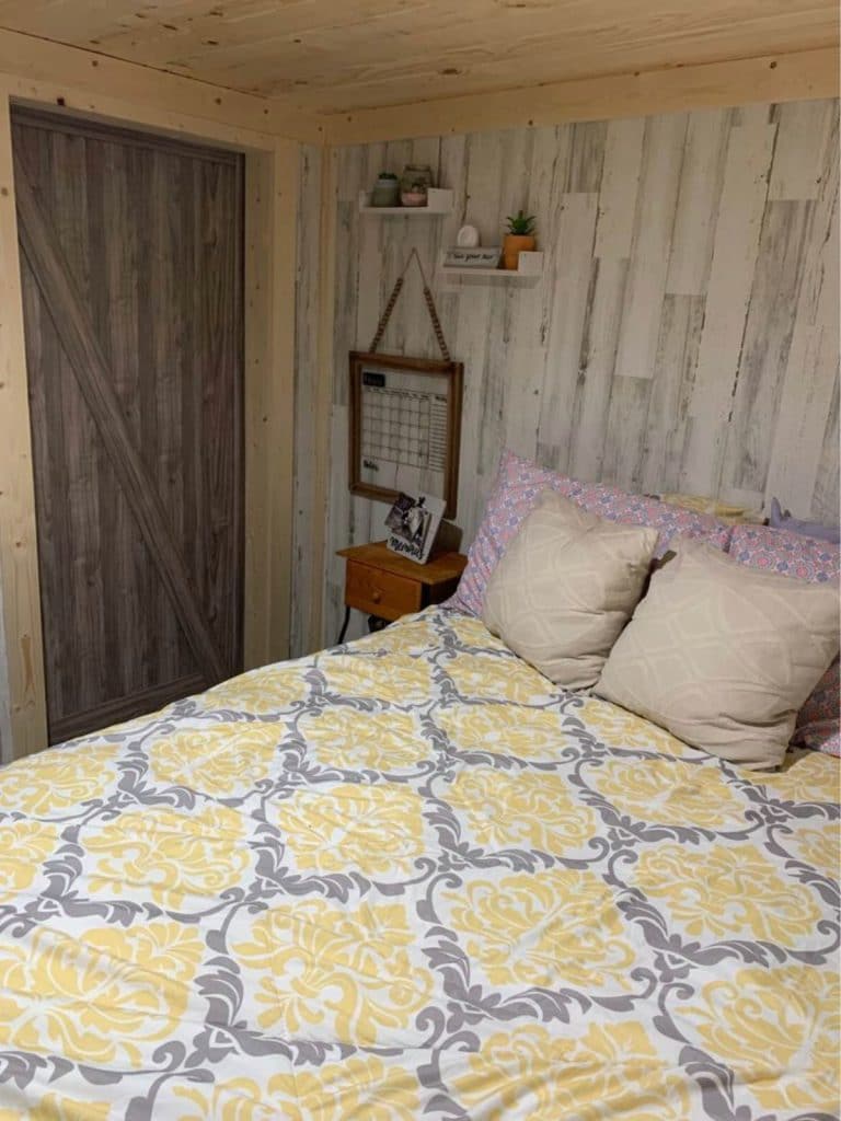 Bed against light wood wall with dark wood door opposite