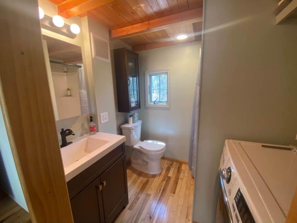 View into bathroom with vanity in foreground and dark wood cabinet above toilet
