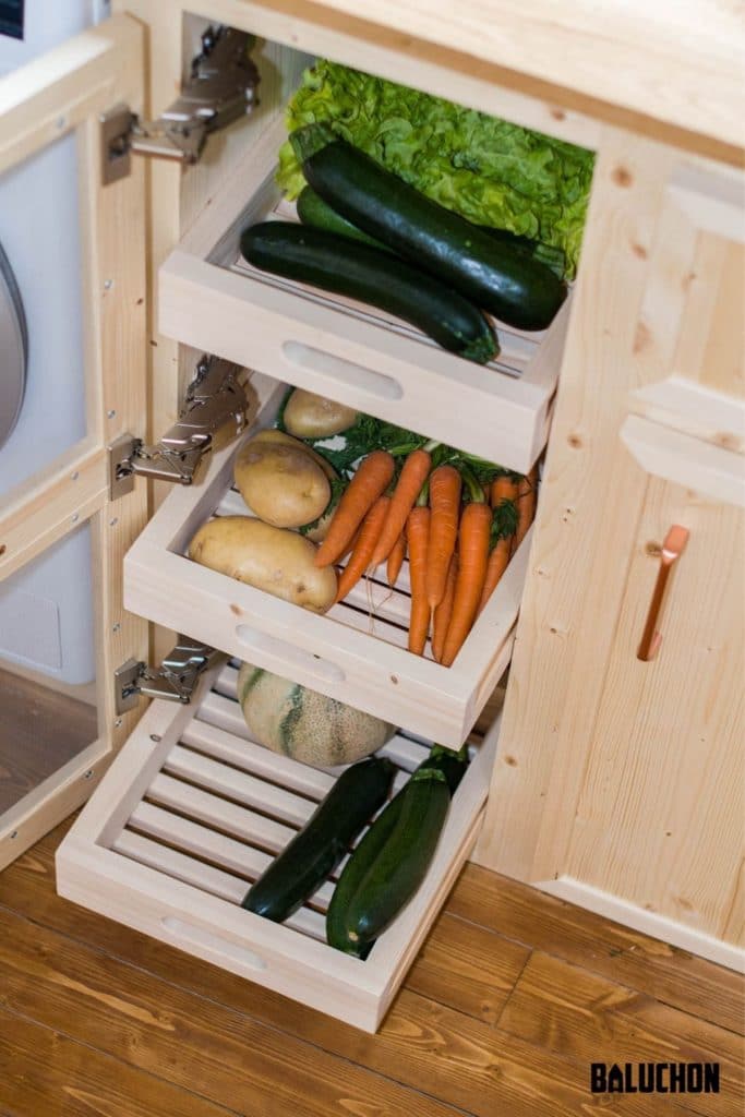 White slotted drawers in cabinet holding vegetables with glass door