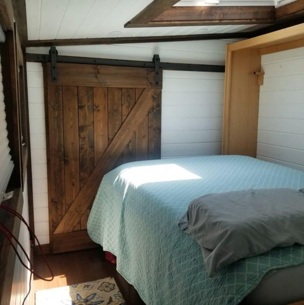 Teal blanket on bed in small room with dark wood barn door closet