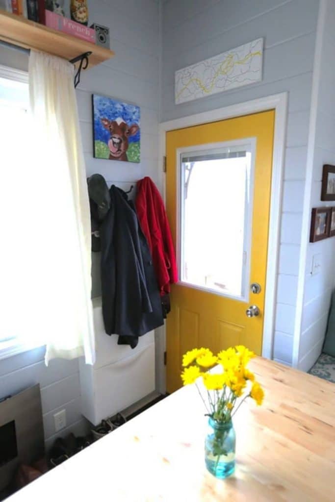 Yellow front door of tiny house with coat rack beside it