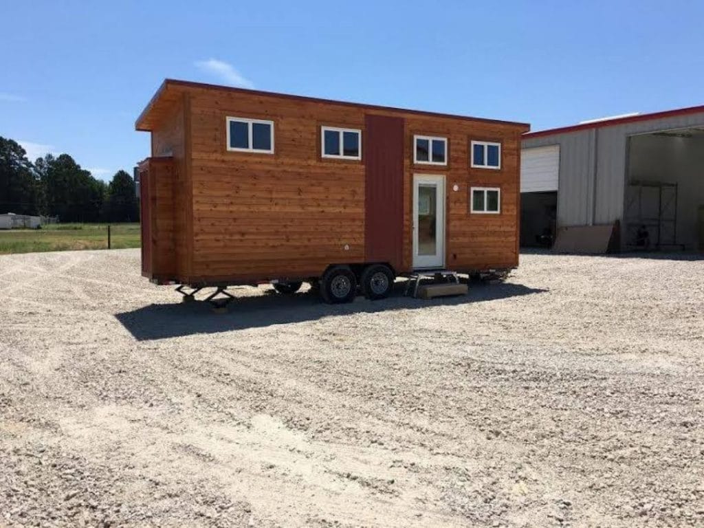 Stained wood siding and white trim on small tiny house on wheels in gravel lot