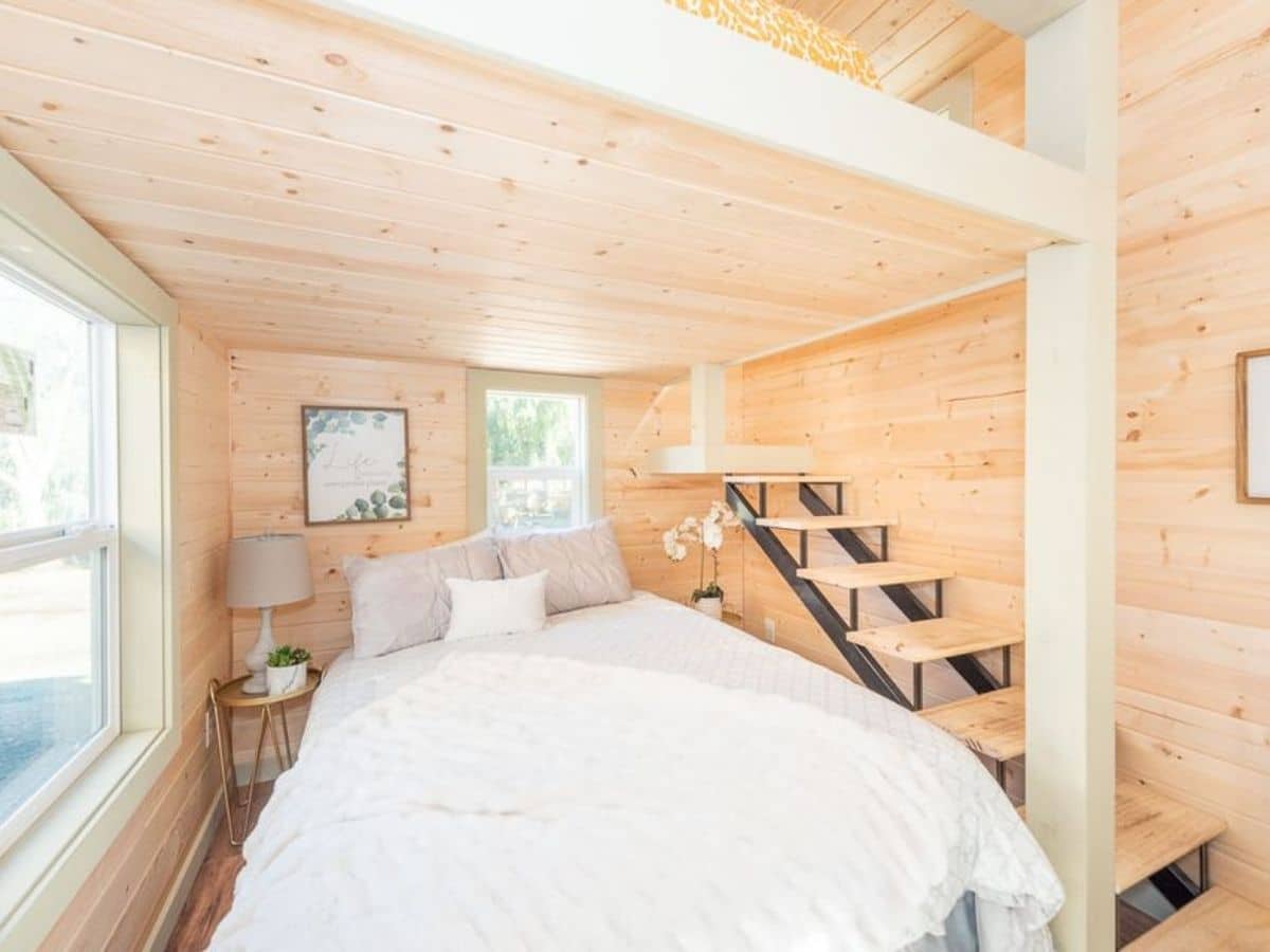 Tiny house bedroom with white bed next to stairs to loft