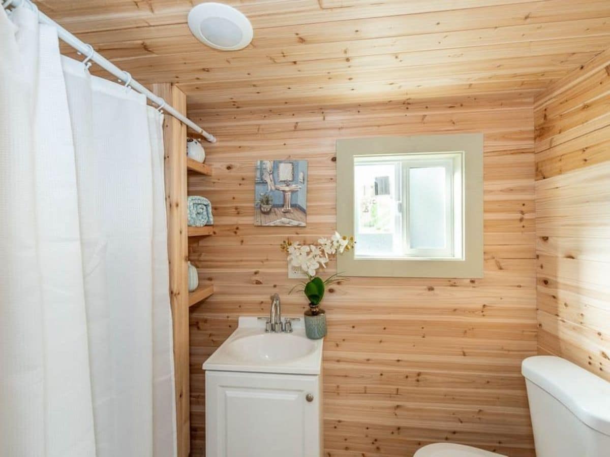 Shower with white curtain on left of bathroom with wood slat walls