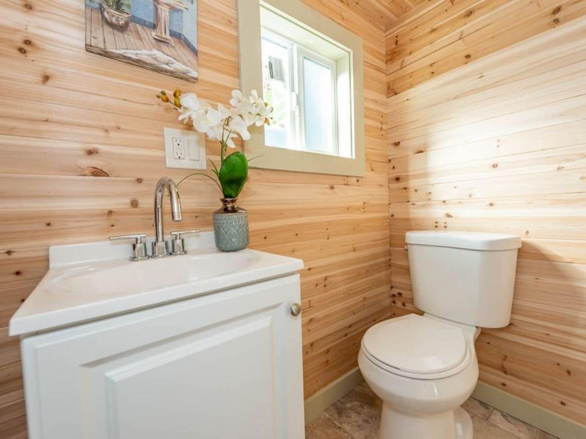 Light wood walls with white flush toilet and white vanity by window