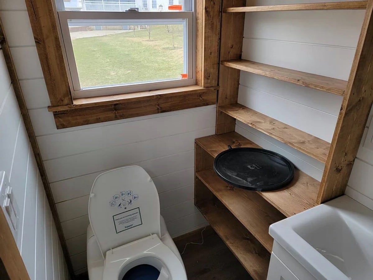 Bathroom showing toilet with open lid next to wooden shelves and white vanity