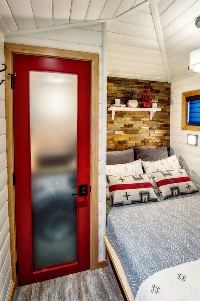 Red trimmed frosted glass door next to bed against fake brick wall