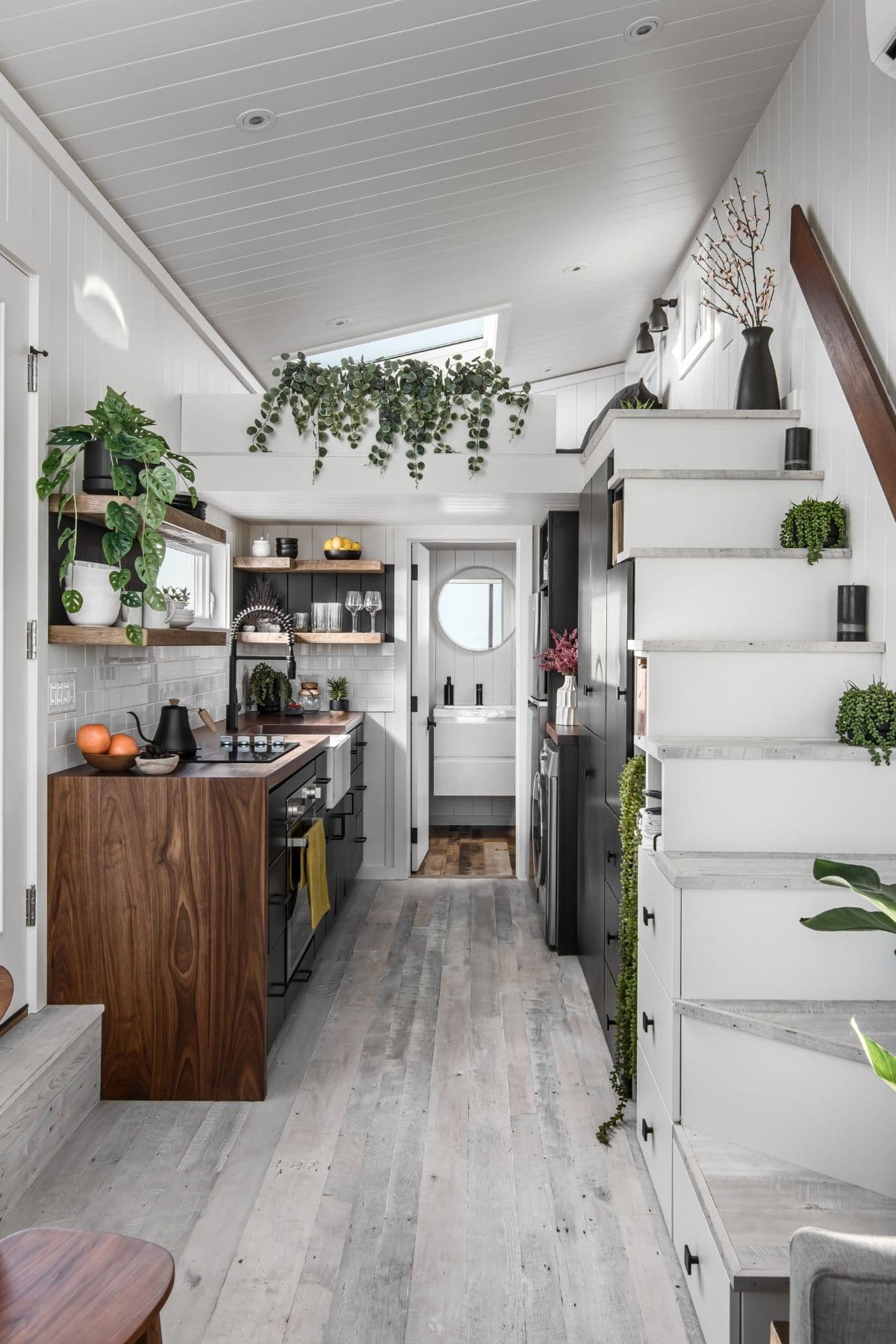 View into tiny home with white stairs to loft on right and kitchen counter on left