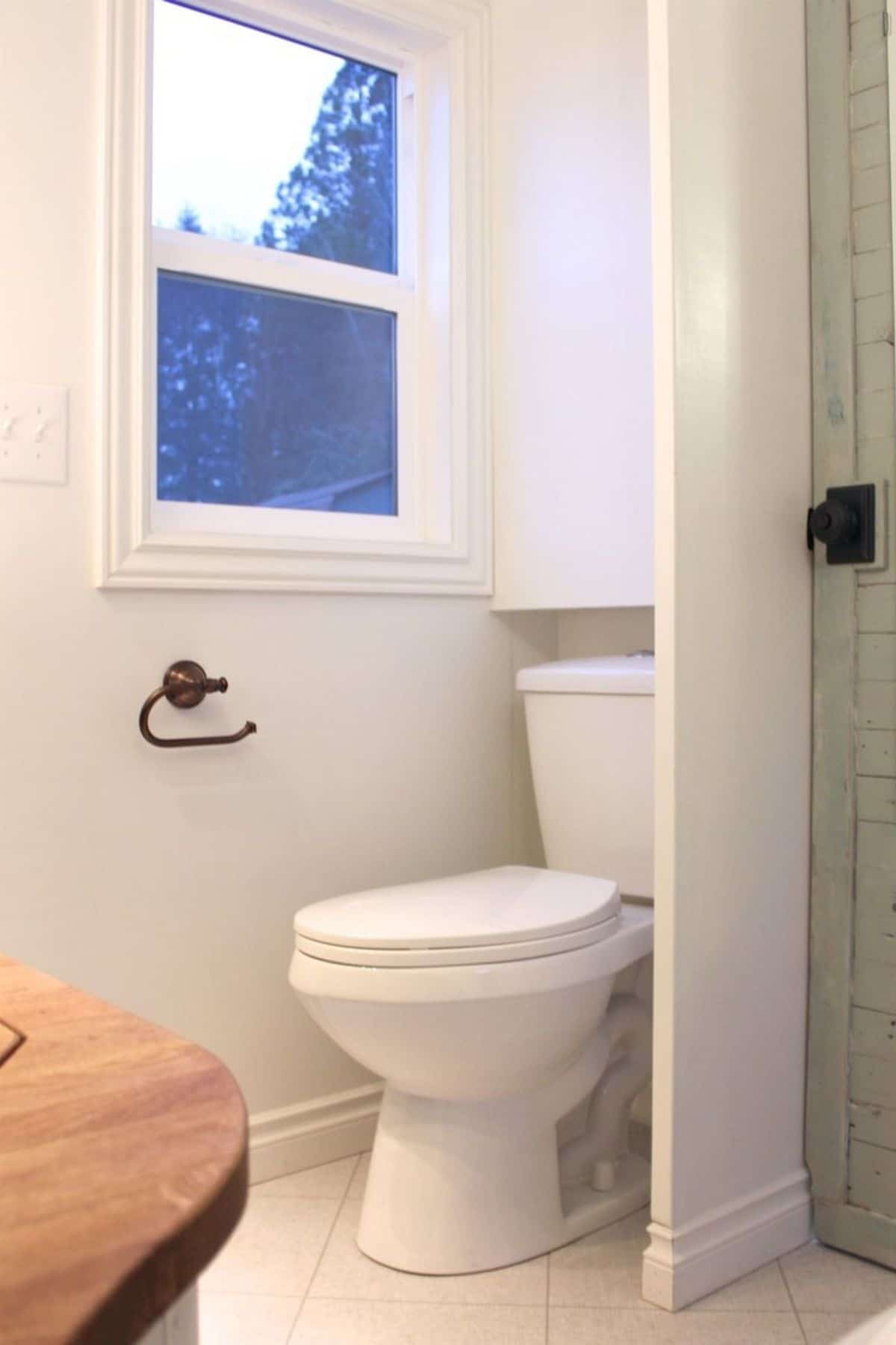 White toilet with white cabinet above inside bathroom door