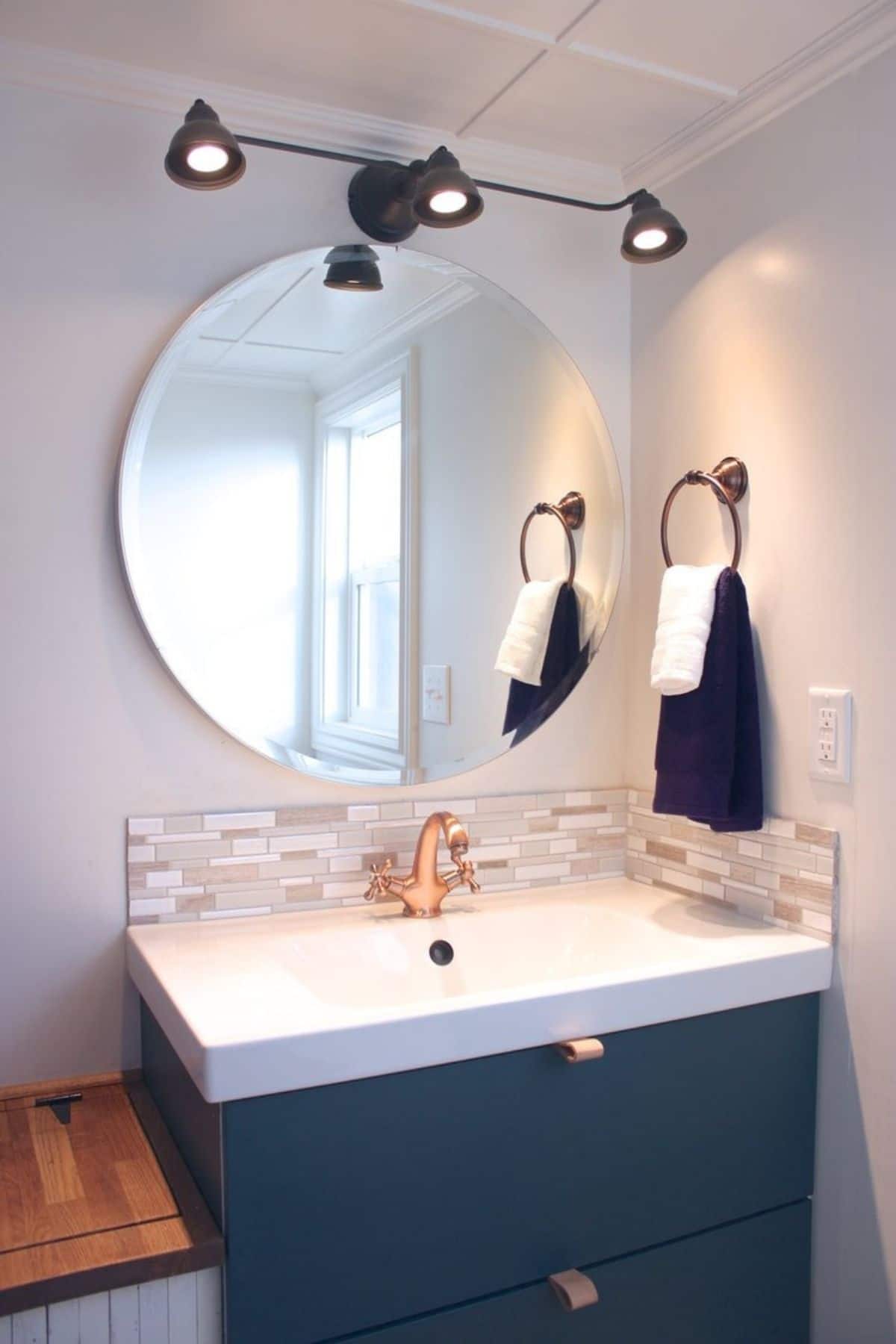 Teal vanity with white sink and round mirror on wall above