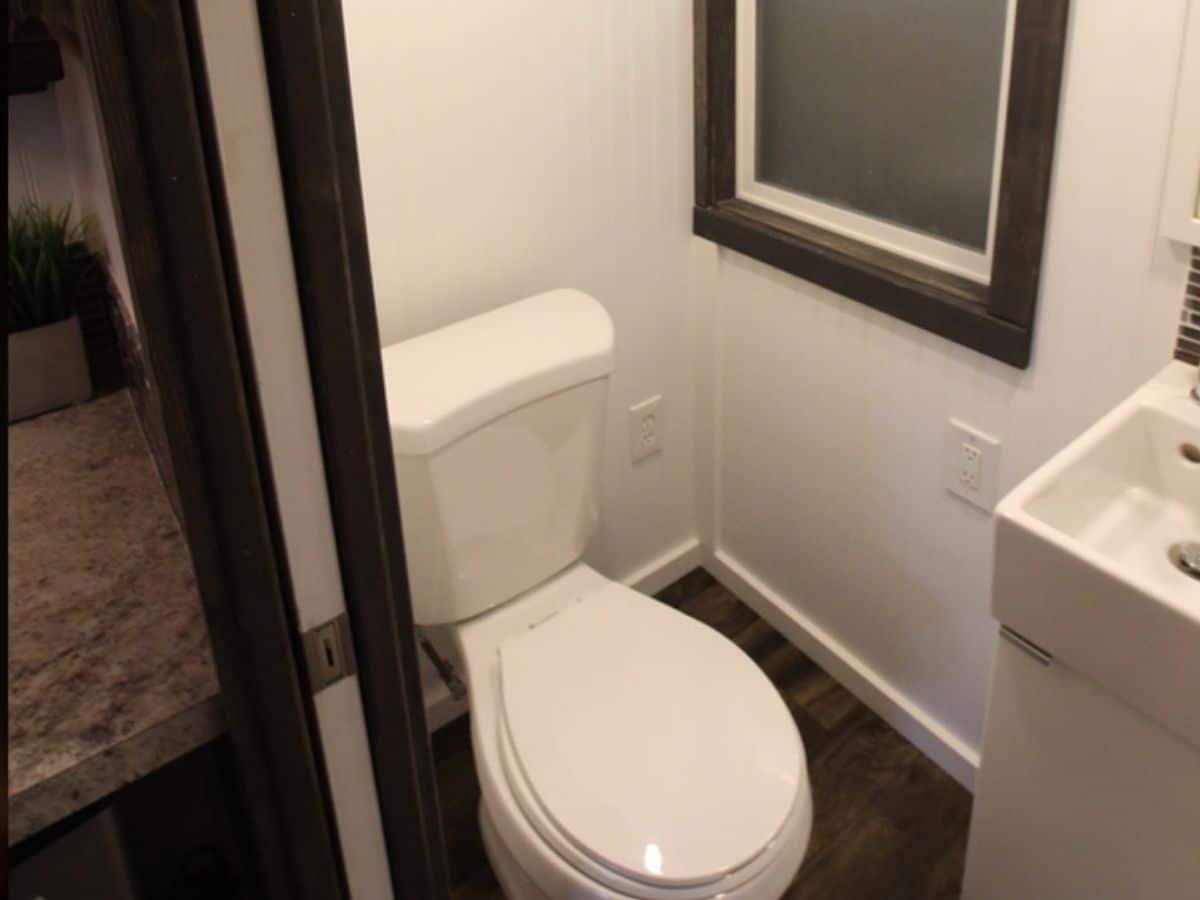 White toilet in walnut flooring by white wall