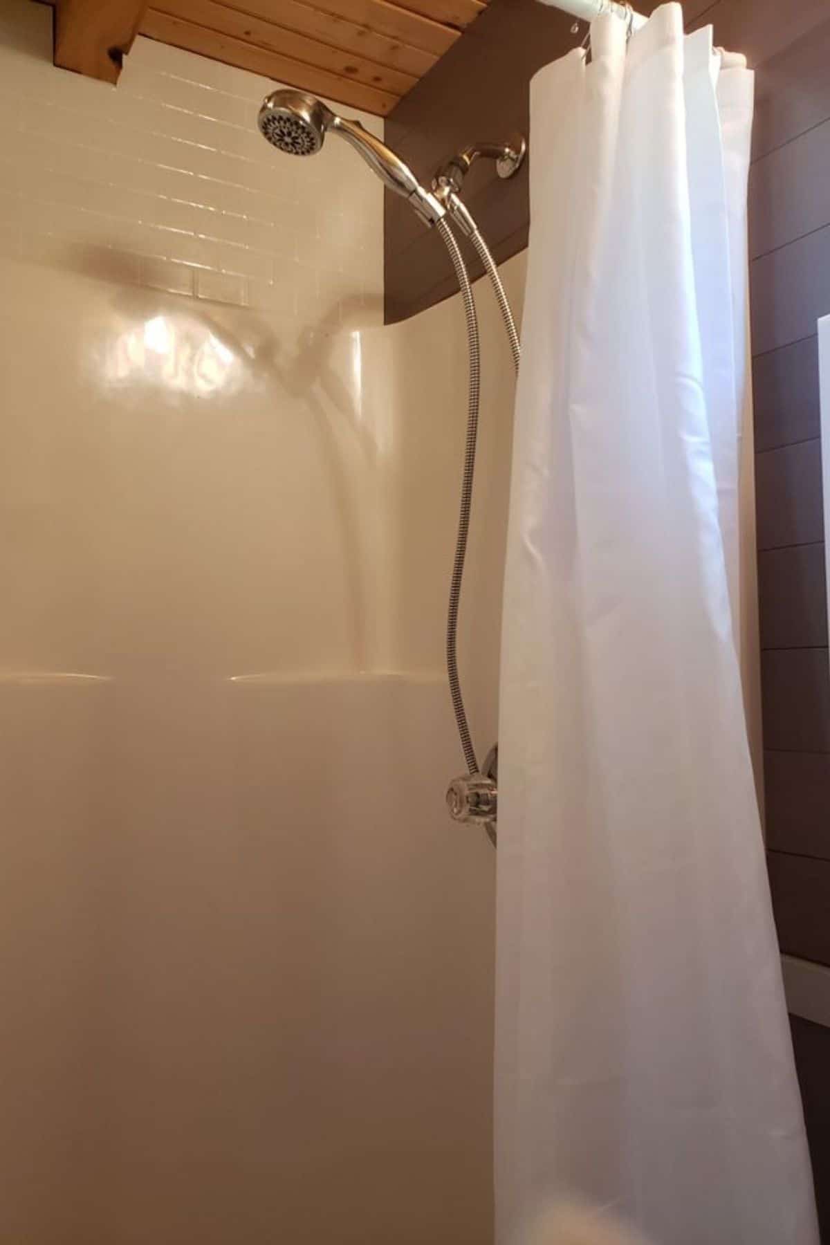 White shower stall with brown wall and white shower curtain