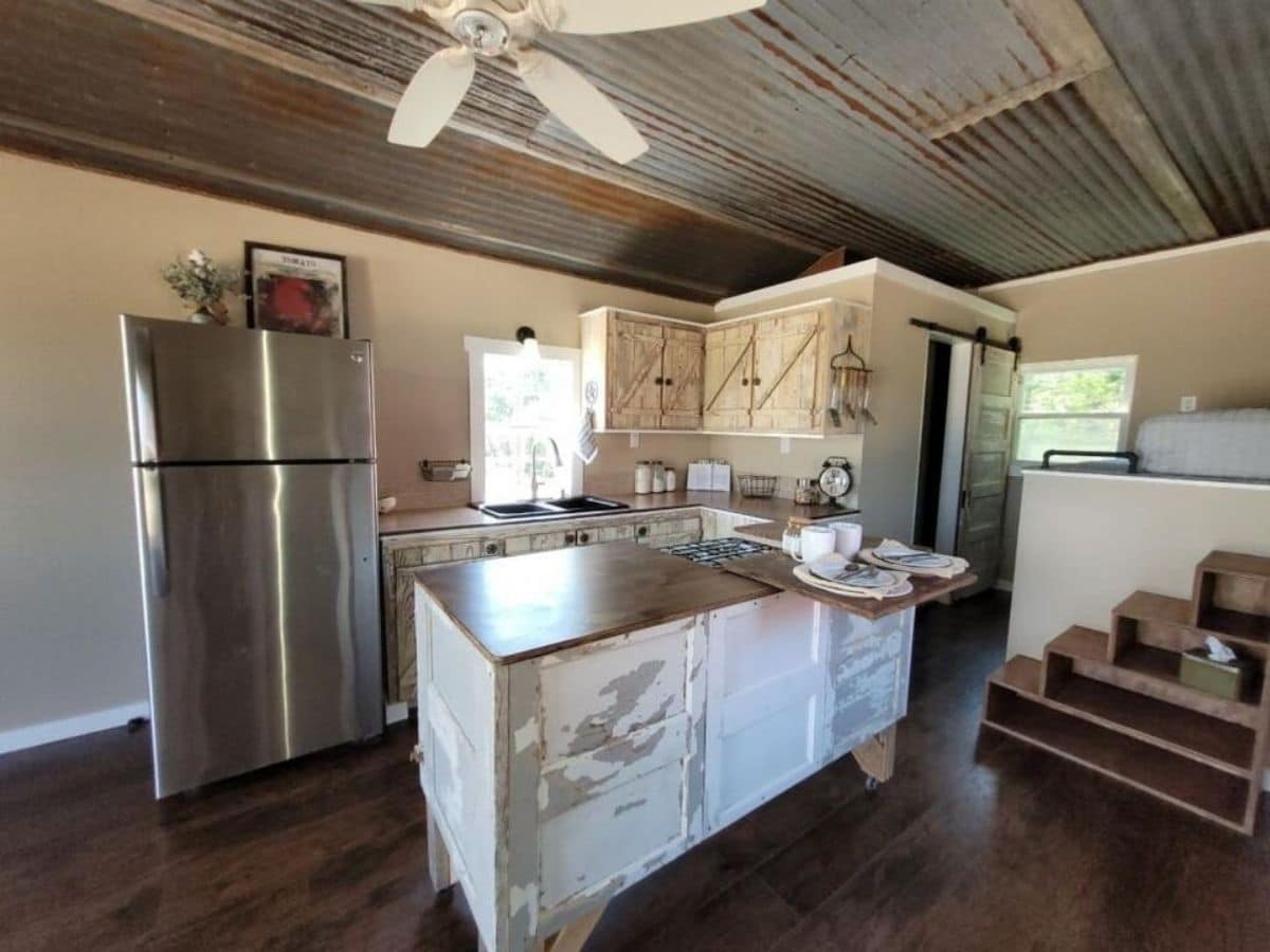 Tiny kitchen with large stainless steel refrigerator and distressed cabinet island