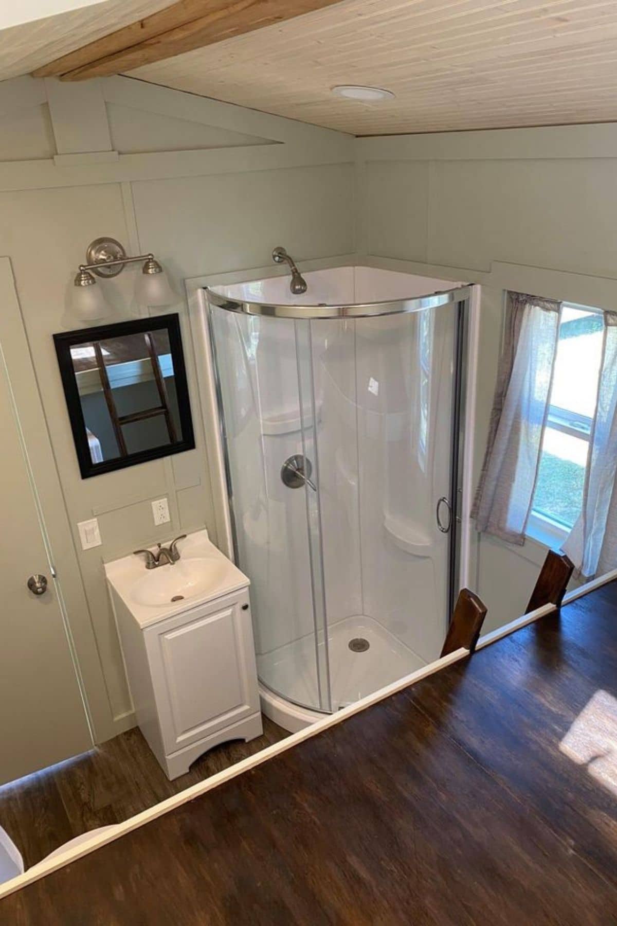 Glass shower in corner next to white vanity with black mirror above
