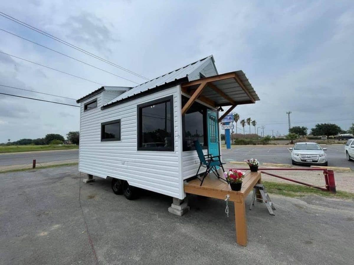 White tiny home on lot with wood porch under awning