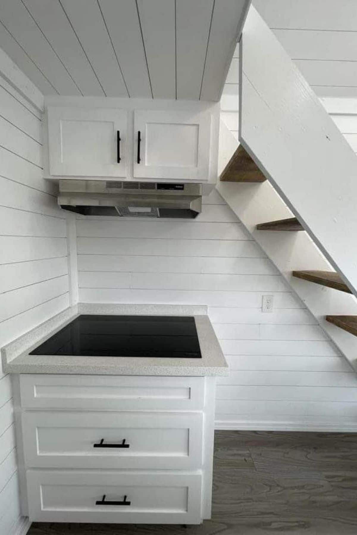 Cooktop in white cabinets under stairs to loft