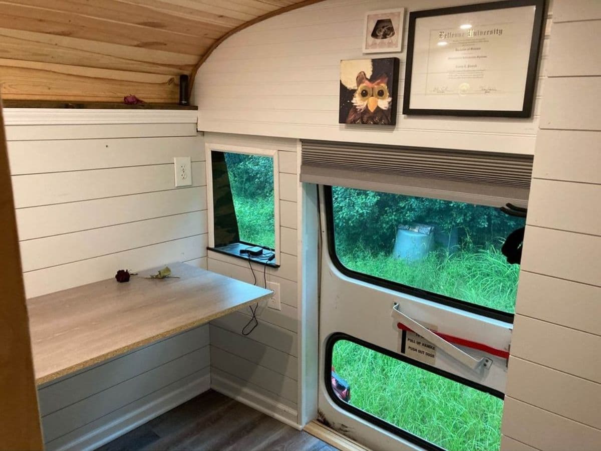 Back door of school bus with desk mounted on wall and white shiplap walls surrounding