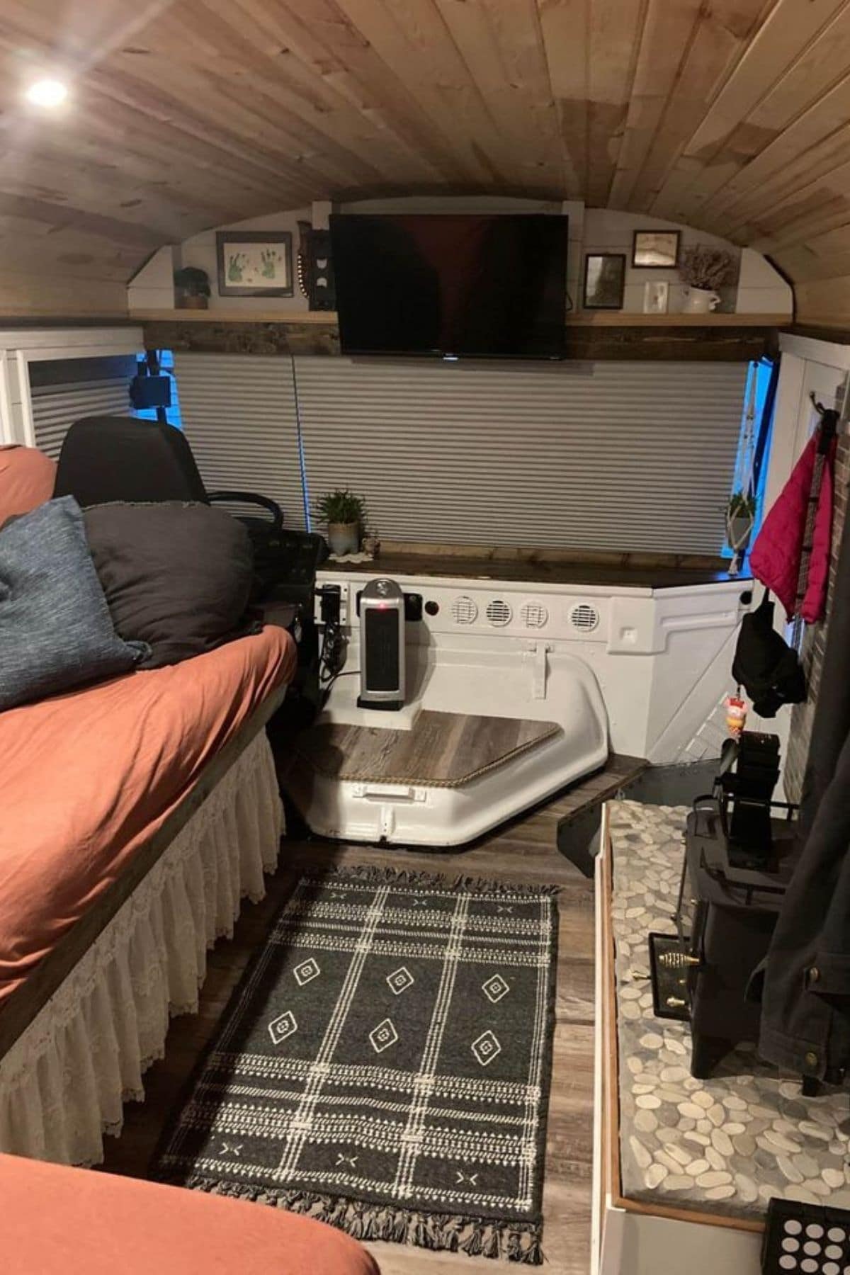 Living area of skoolie with bed on left and clothing on right