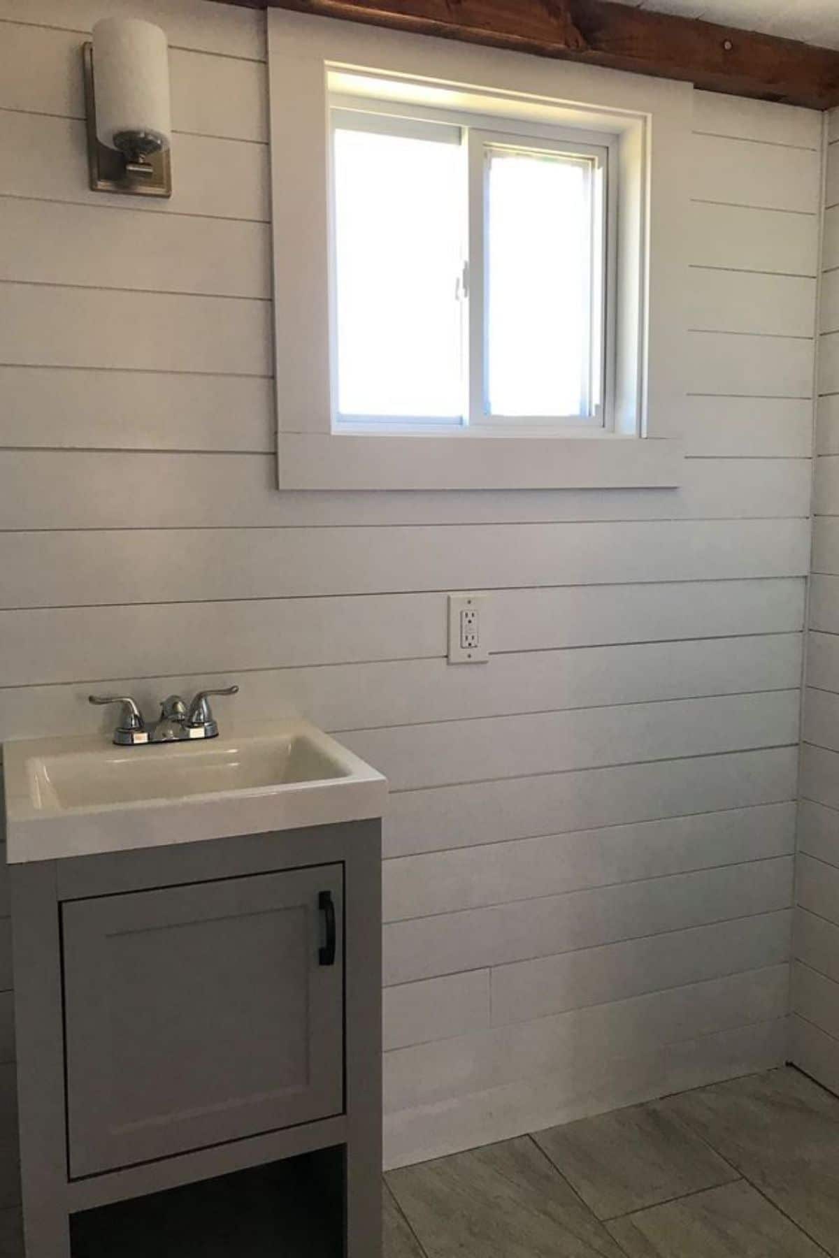 Gray cabinet with white sink above against white shiplap walls