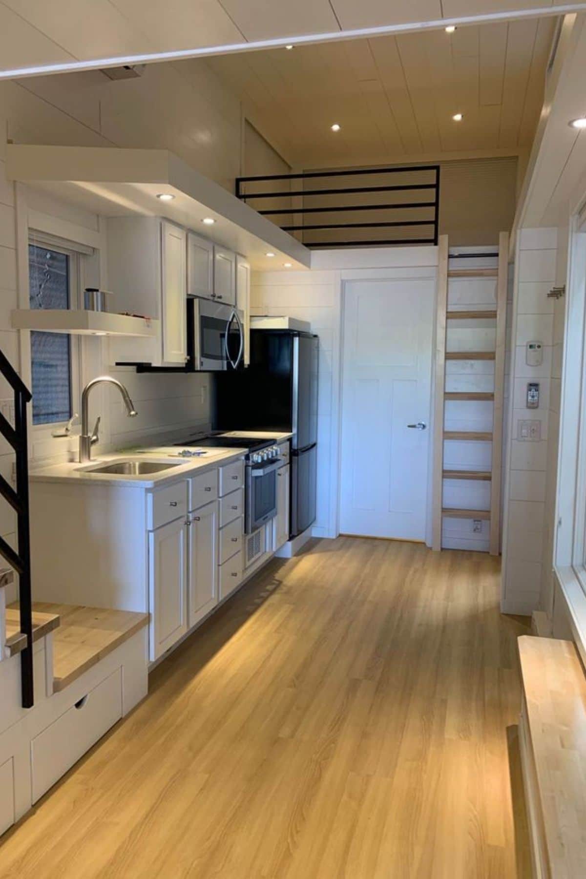 Tiny home kitchen and door to bathroom showing loft with wood ladder above bathroom
