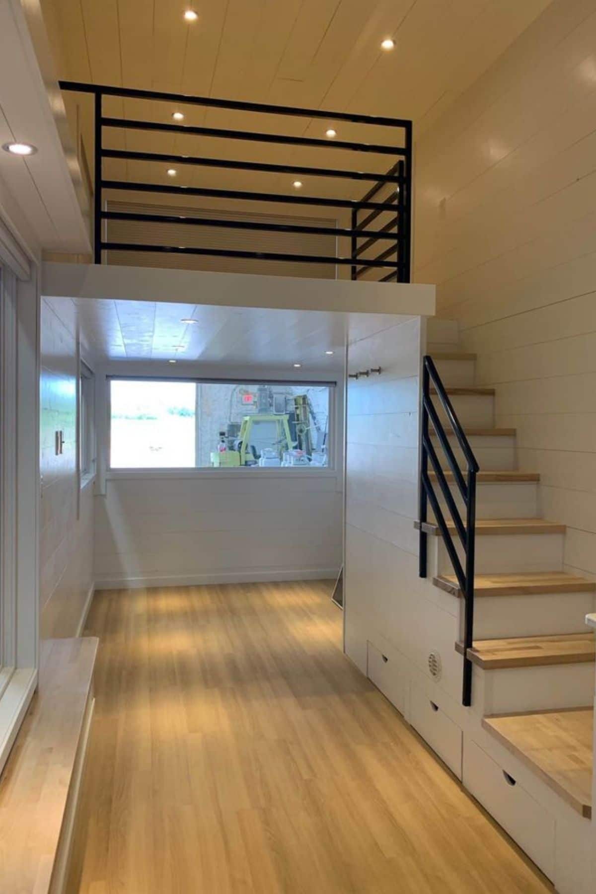 Empty tiny home with light wood floors and white walls and black metal stair railing