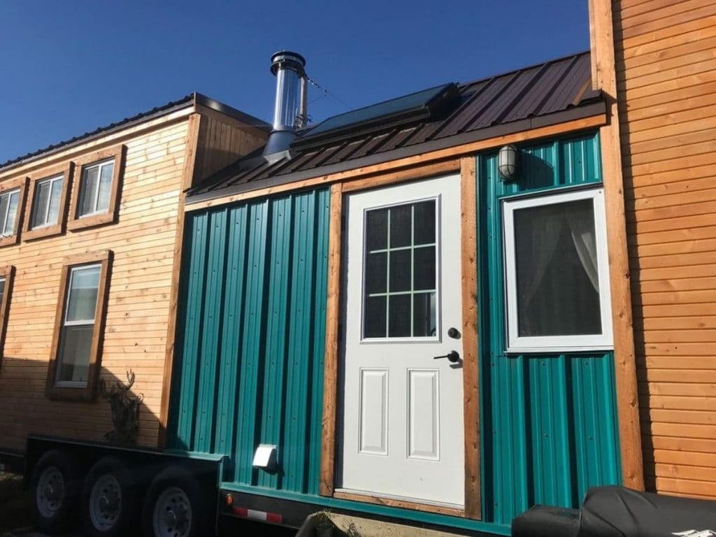White front door in between wood and teal siding on tinyhome