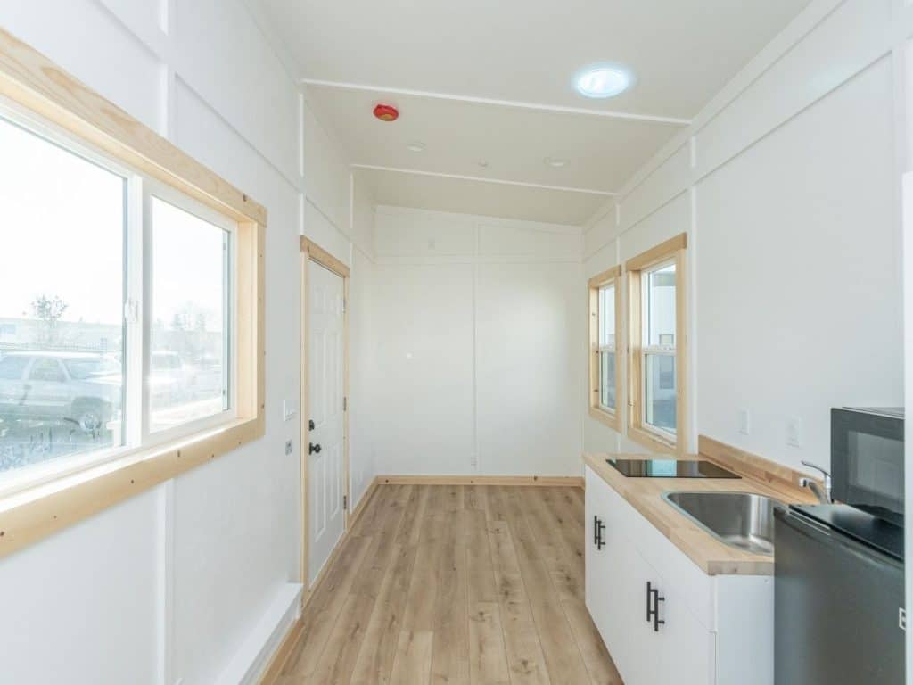 View from tiny bathroom to living area in white tiny home walls with wood floors