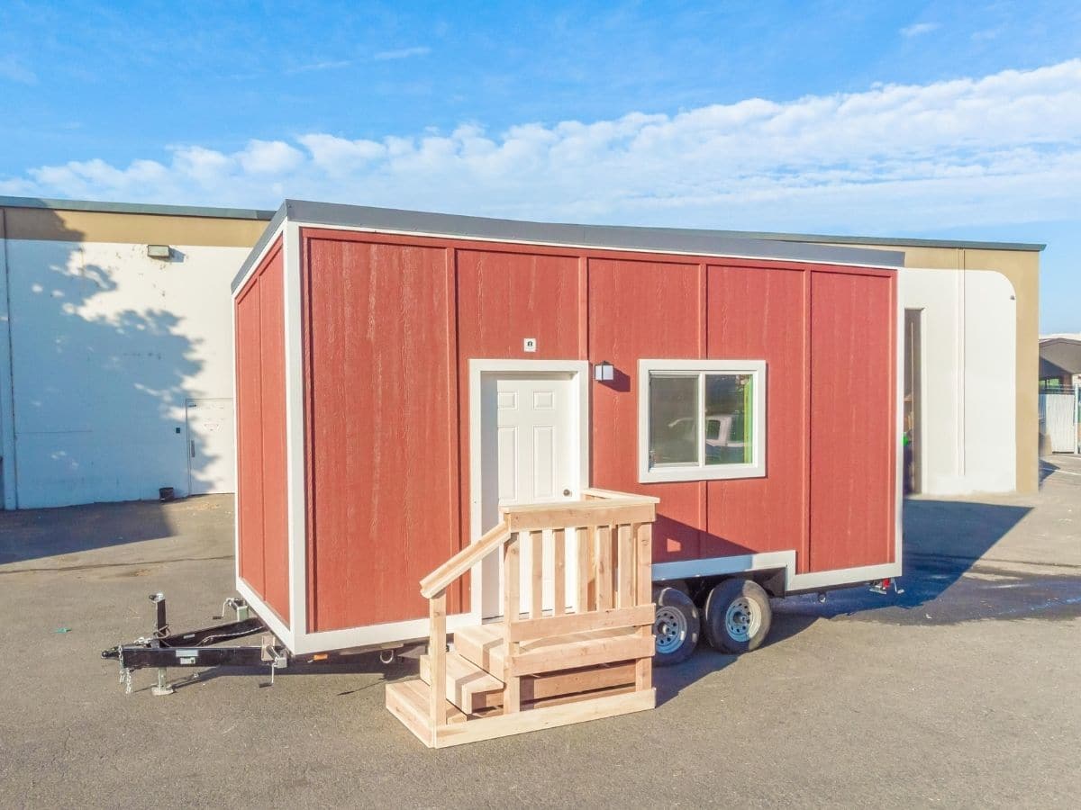Red tiny house with white trim and small wood porch on lot