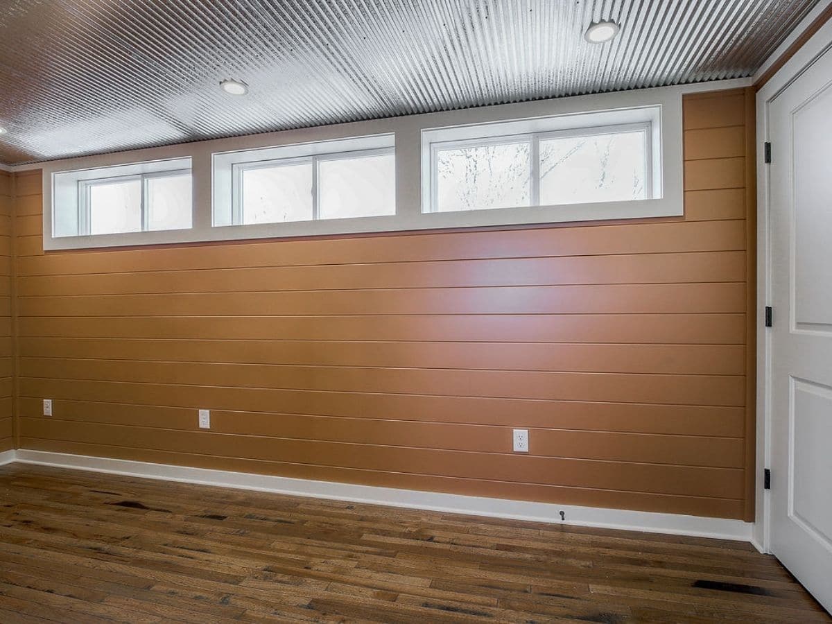 Orange wall and wood floors with three large windows on top of wall