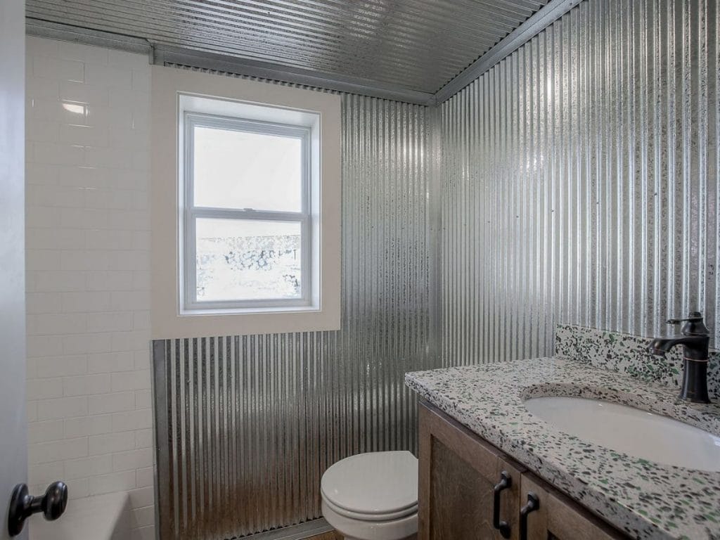 Corrugated metal wall in bathroom with sink in foreground and white toilet