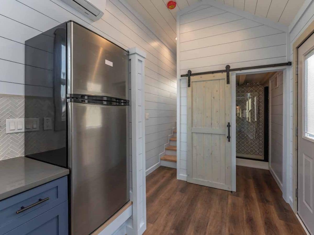 Open door to bathroom next to loft stairs with stainless steel refrigerator in foreground