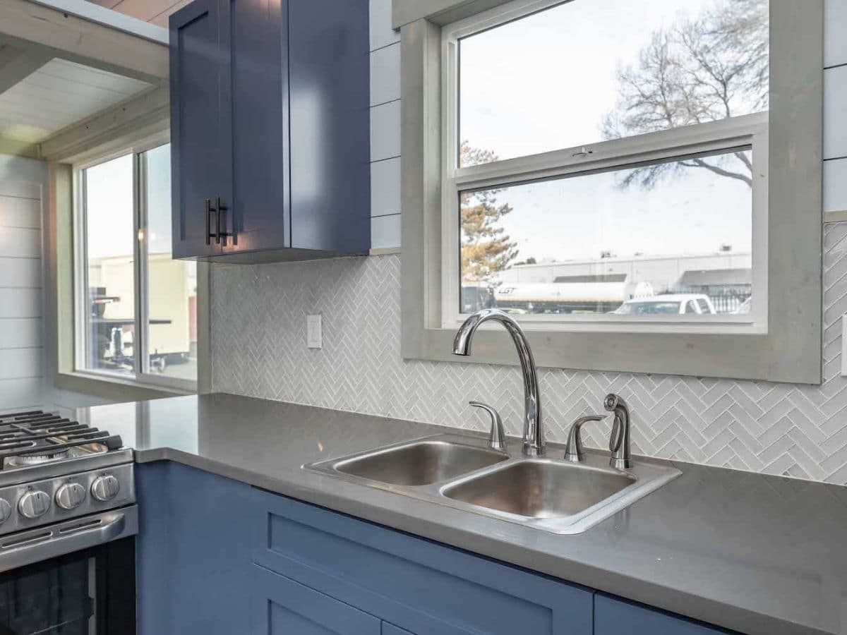 Gray countertop on blue cabinets in tiny home with sink below window