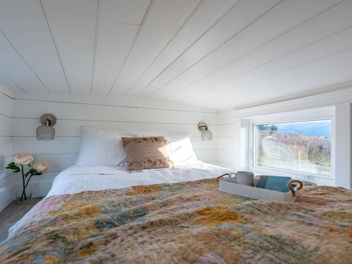 Bed with colorful blanket in loft by large window and low ceiling