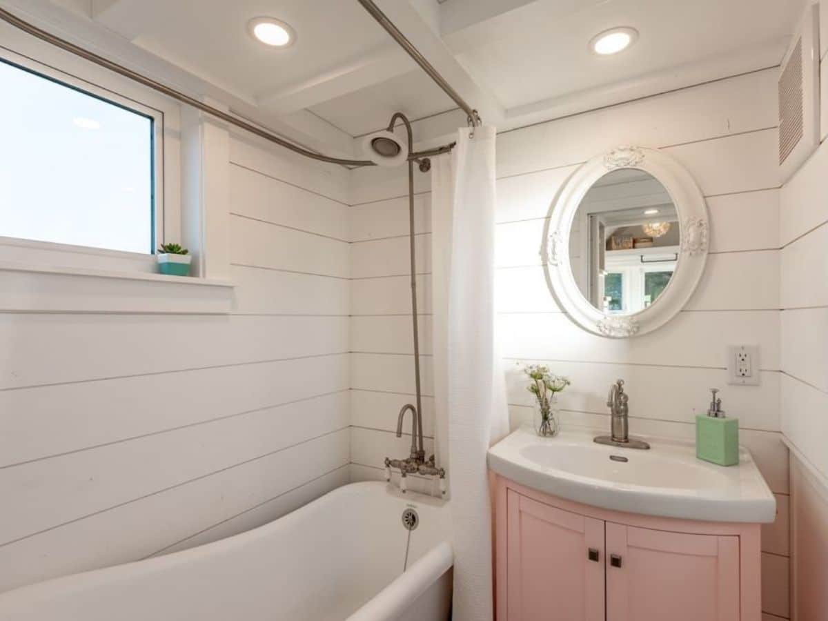 Clawfoot bathtub against white shiplap wall in bathroom with pink vanity
