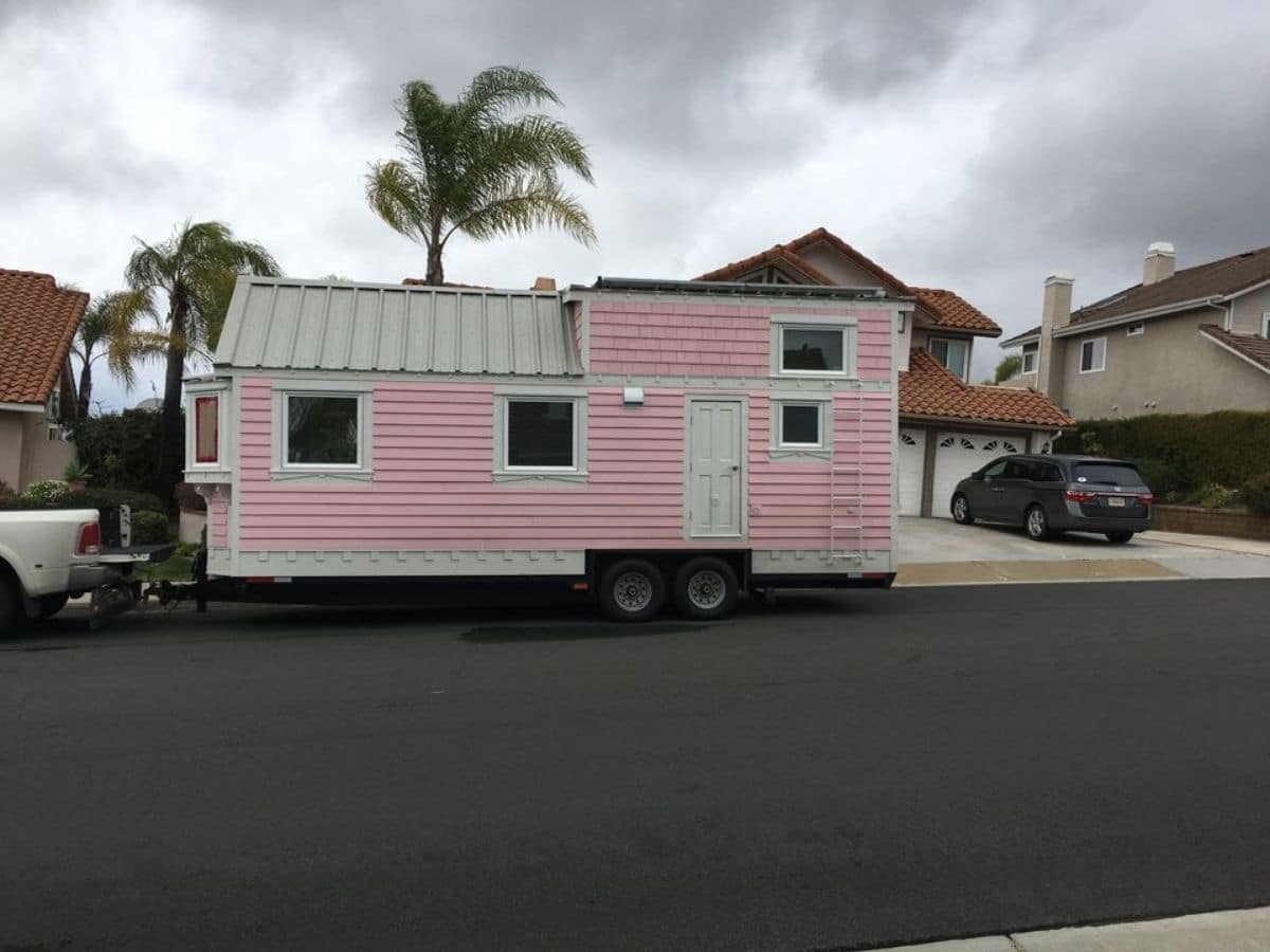 Pink and white tiny home parked in front of driveway of home