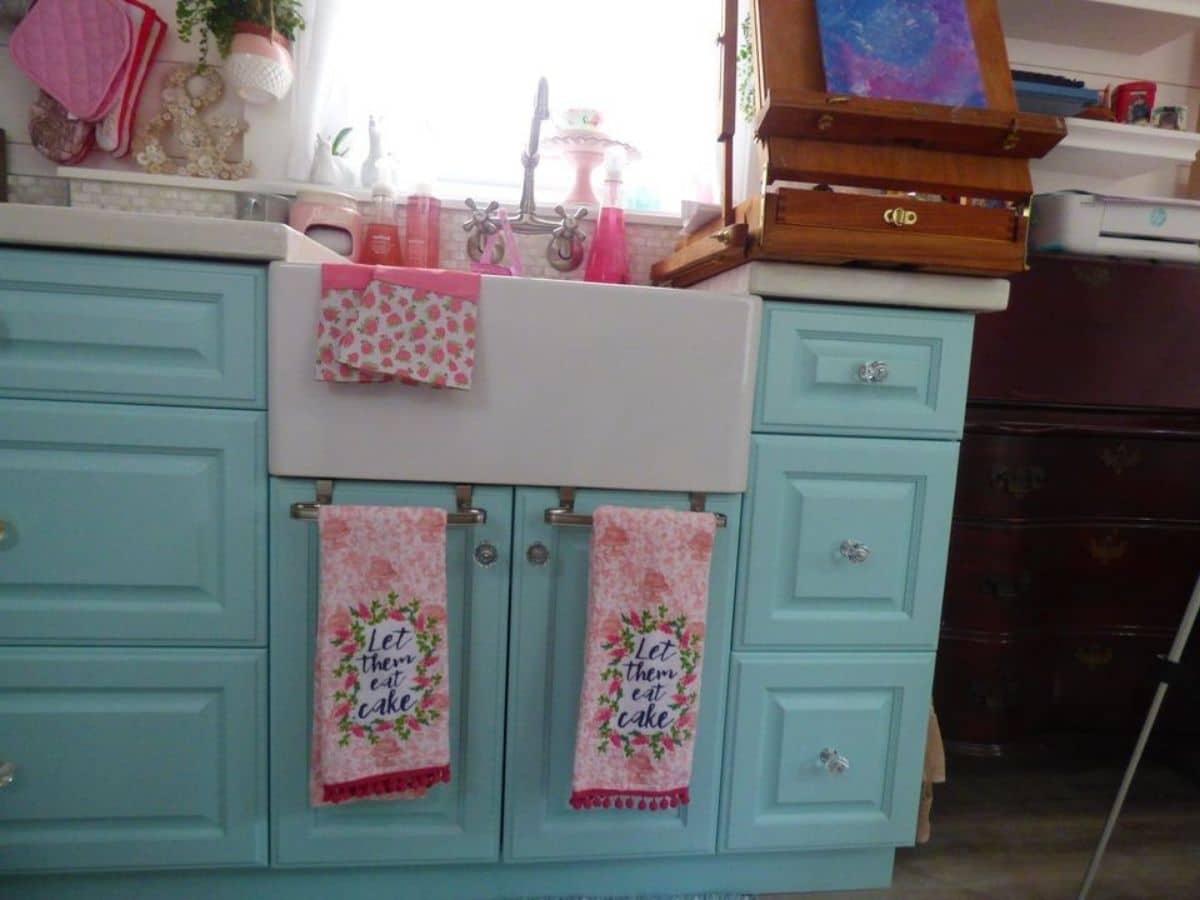 Pink hand towels handing on teal cabinet doors under white farmhouse sink
