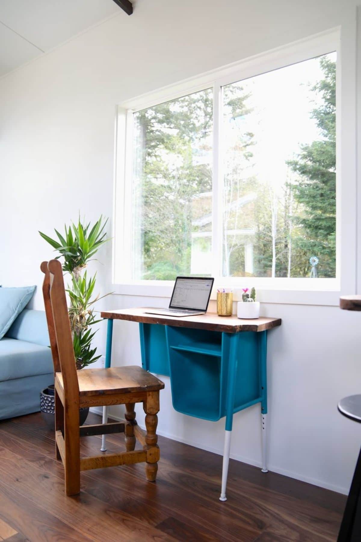 Teal writing desk with wooden chair below large picture window in white wall