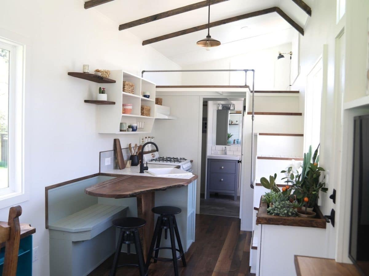 Light gray bench seat and wood table on edge of kitchen in tiny home