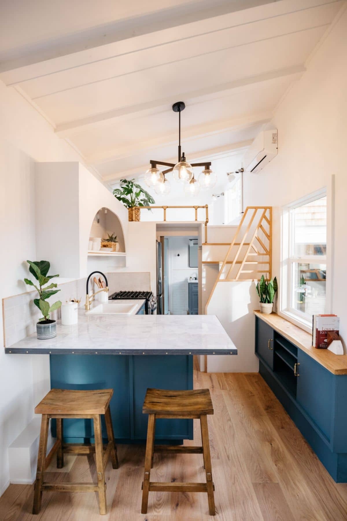 Teal cabinets in kitchen of tiny home with wood stools in foreground