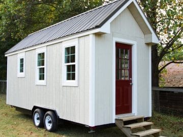 White tiny home with red door and wood steps