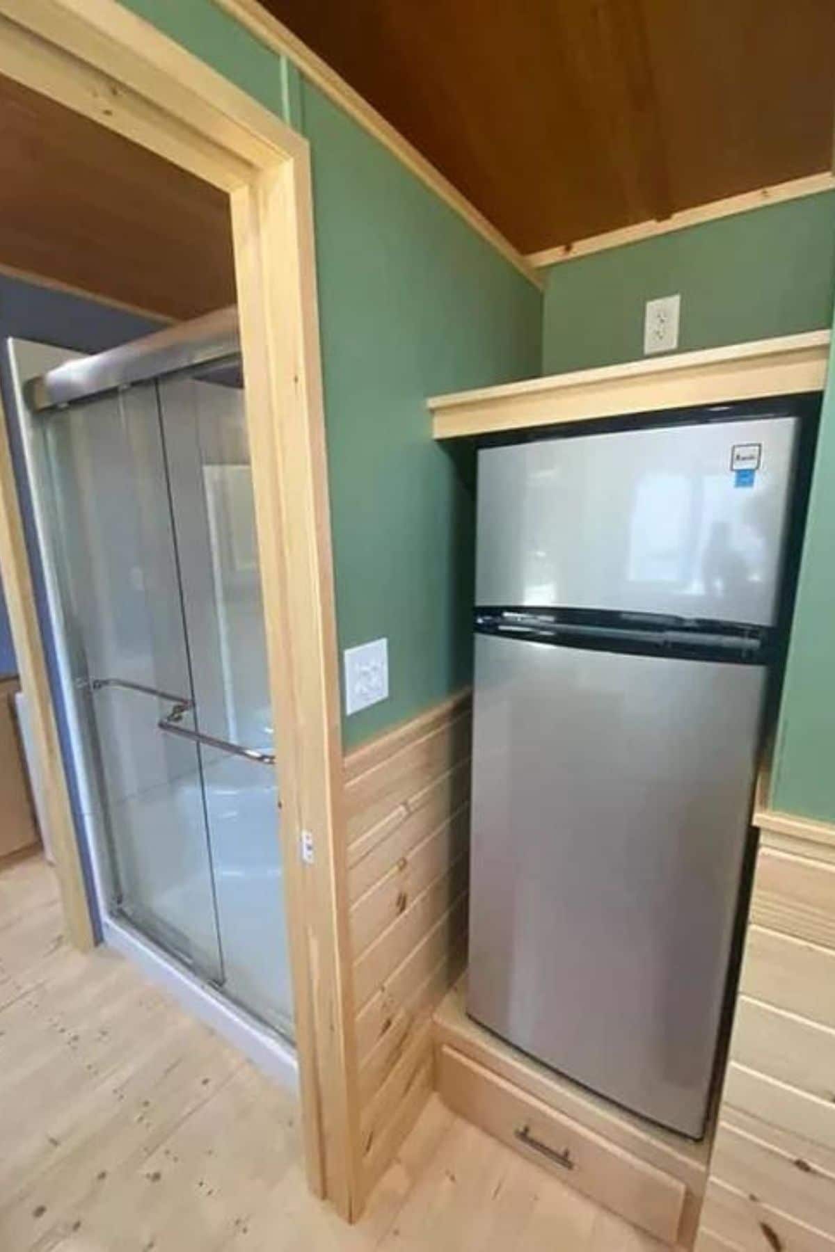 Stainless steel refrigerator under cabinet next to wall by bathroom