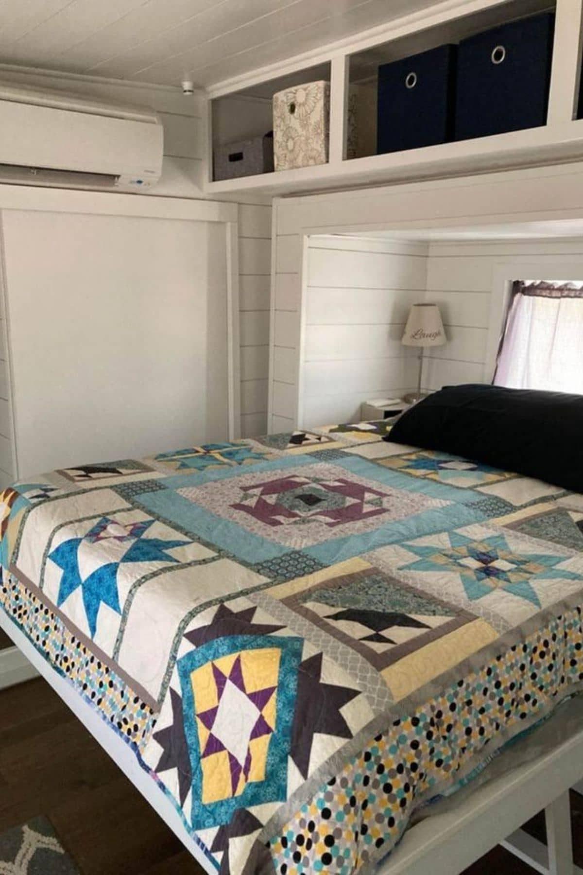 Colorful quilt on bed tucked into slide out of tiny home with white shiplap walls