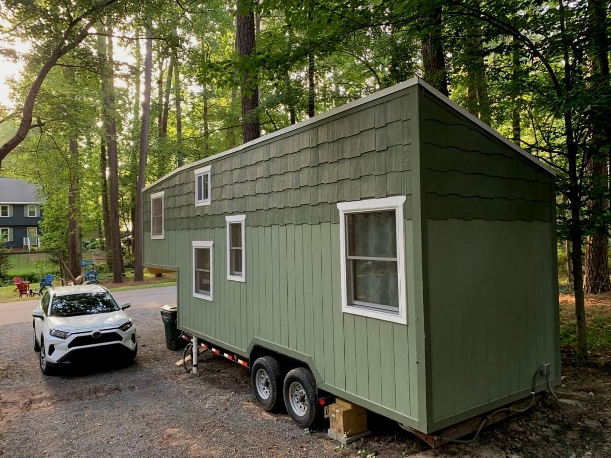 Two toned green tiny home on wheels by white car