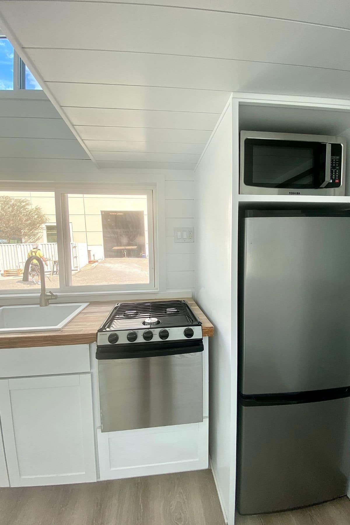 Stainless steel refrigerator in white cabinet next to rv sized stove by white sink