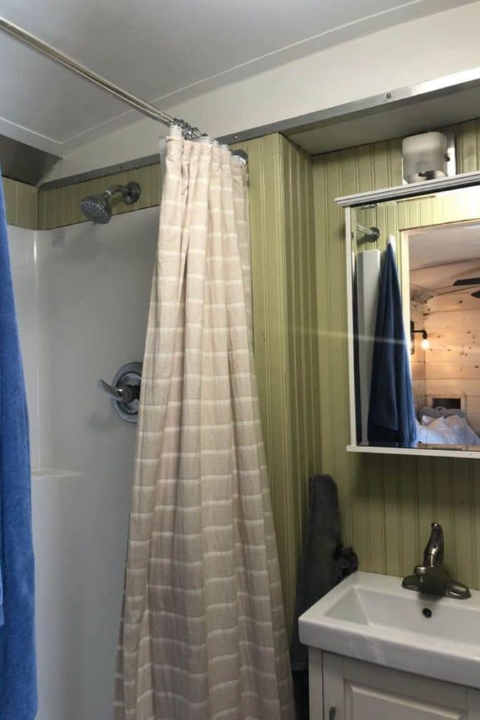 Green bathroom walls with white shower on left and sink with mirror above on right of image