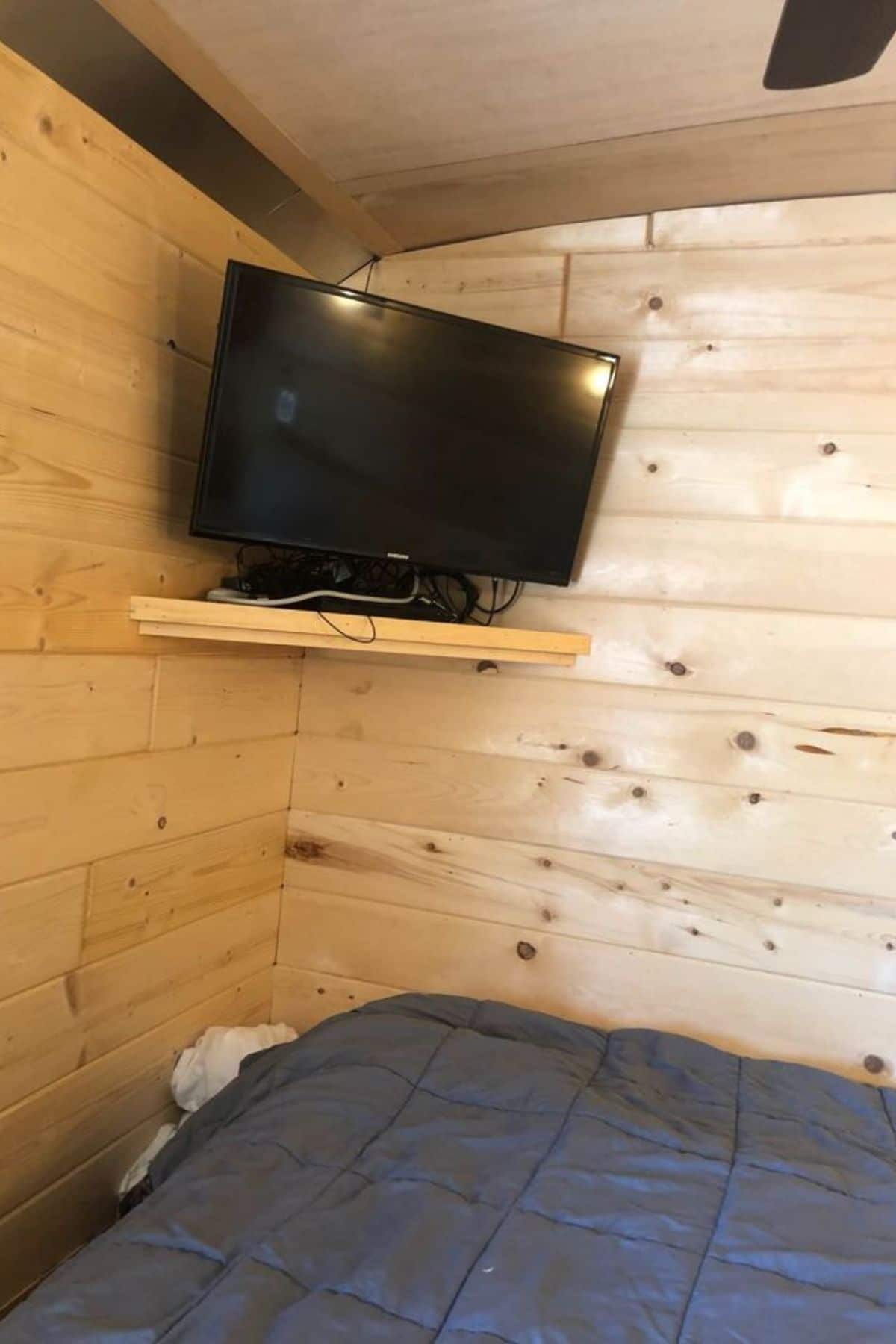 Light wood walls with shelf holding small television in corner